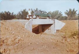 Fotografía de un auto sobre el puente junto a un hombre. Atrás indica "Puente canal A-1-2"