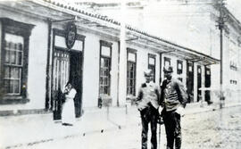 Fotografía con la imagen de dos policías situados frente a dos edificios no identificados. Aparec...