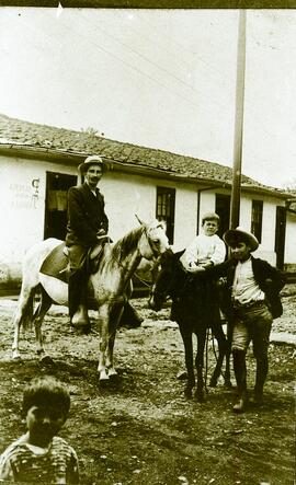 Fotografía de hombre a caballo y niños, se observa una pulpería y taquilla al fondo
