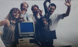 Fotografía de publicidad con chimpancé posando con cuatro personas junto a una computadora