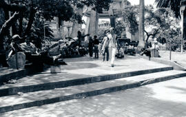 Fotografía con la imagen de un limpiabotas en el Parque Central de San José Al fondo se observa e...
