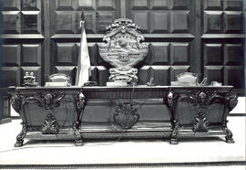 Fotografía de la mesa del Directorio de la Asamblea. Es un mueble tallado en caoba por los trabaj...