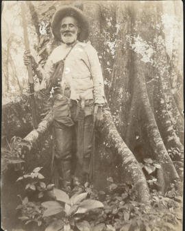 Fotografías de un hombre anciano junto a un árbol, en un lugar boscoso. Sostiene en su mano un ri...