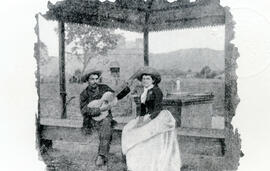 Fotografía de una pareja de músicos nativos, sentados en la banca de un kiosko, ubicado en la pla...