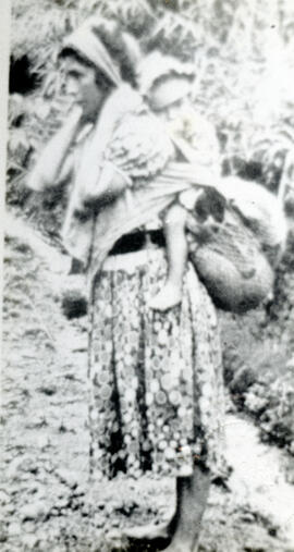 Fotografía de una mujer indígena de la Región Talamanca. Carga a su hijo y otros objetos sobre su...