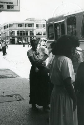 Fotografía con la imagen de una mujer con vestimenta larga, llevando una niña en brazos. Hace fil...