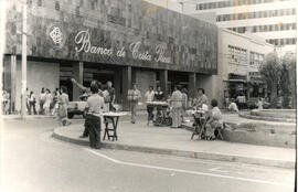 Fotografía con la imagen del edificio del Banco de Costa Rica, y venta de lotería en la avenida c...