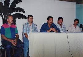 Fotografía de cinco hombres sentados y Jorge Sauma Aguilar, gerente general, hablando por micrófo...