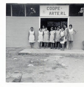 Fotografía de un grupo de personas y mujeres posando a la entrada de Coope Arte R.L., se aprecian...