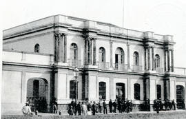 Fotografía con la imagen del edificio de una mansión ejecutiva. Aparece un grupo de hombres junto...