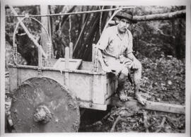 Fotografía de un boyero-campesino con sus piernas embarrialadas, sentado en la parte delantera de...